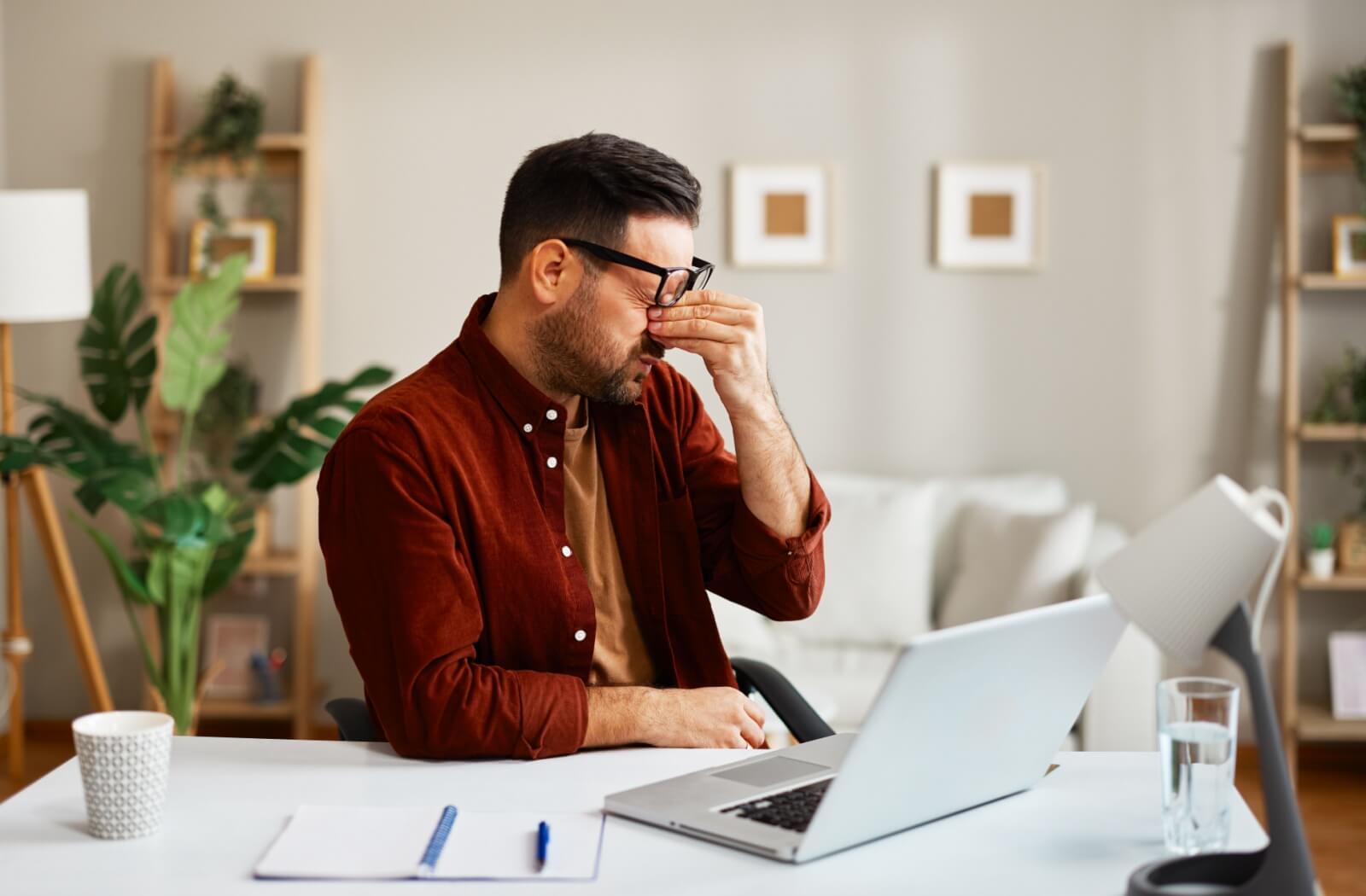 A person wearing glasses sits at a desk with a laptop.