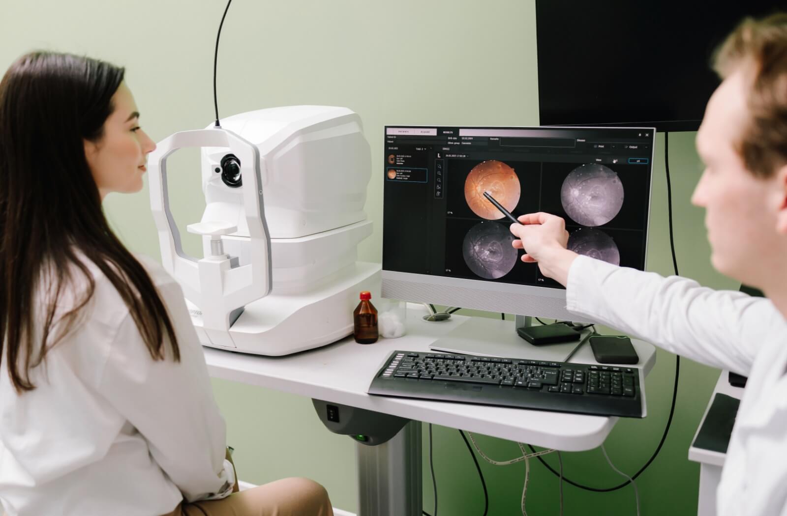 An eye doctor pointing to digital retinal scans on a monitor to explain how fast macular degeneration progresses to a patient.